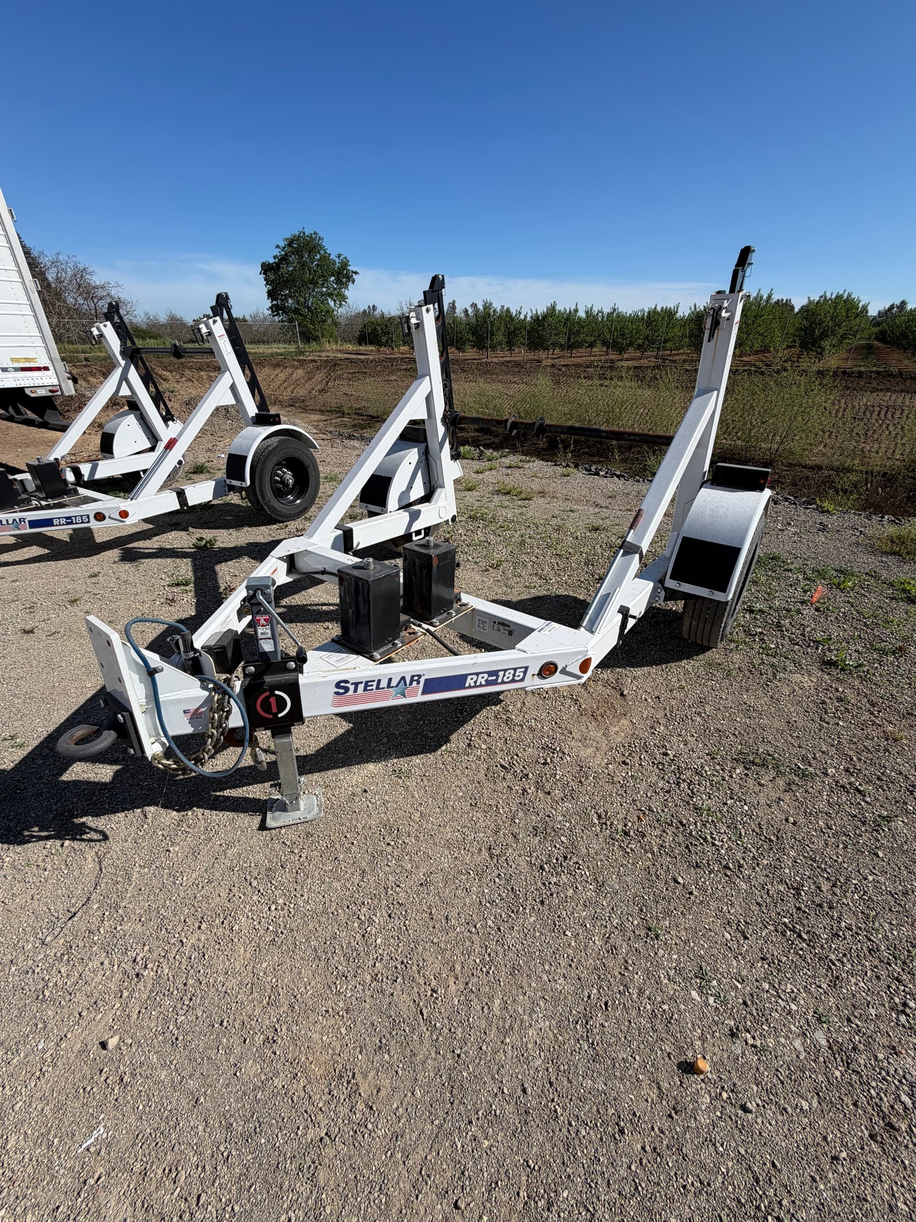 Stellar RR-185 cable reel trailer on the FleetWay yard, reel arms raised, with a second unit and an orchard behind it